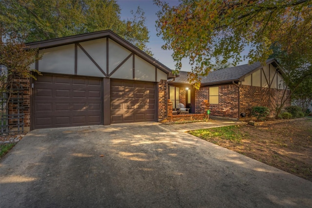 english style home with a garage, brick siding, concrete driveway, roof with shingles, and stucco siding