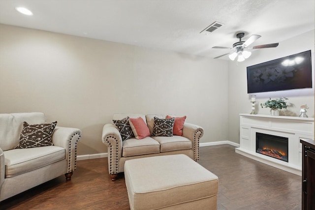 living area featuring a glass covered fireplace, dark wood finished floors, visible vents, and baseboards