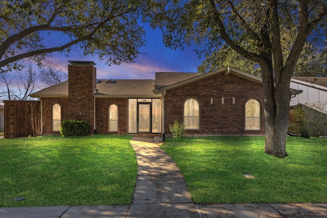 single story home featuring brick siding, roof with shingles, a chimney, and a lawn