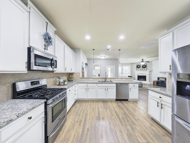 kitchen with a fireplace, stainless steel appliances, open floor plan, a sink, and a peninsula