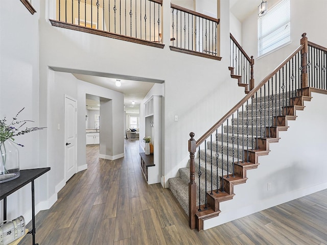 staircase with a towering ceiling, baseboards, and wood finished floors