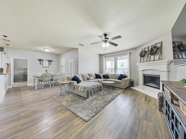 living area with a fireplace with raised hearth, wood finished floors, visible vents, and a ceiling fan