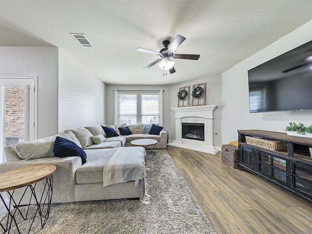 living room featuring visible vents, a fireplace with raised hearth, ceiling fan, a textured ceiling, and wood finished floors