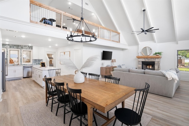 dining area with light wood finished floors, high vaulted ceiling, and a stone fireplace