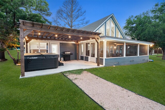 rear view of house with a lawn, a hot tub, a sunroom, a patio area, and a pergola