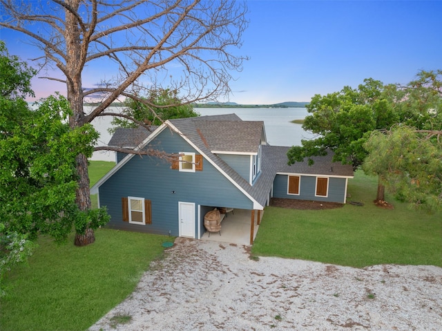 view of front of property with driveway, roof with shingles, a front yard, and a water view