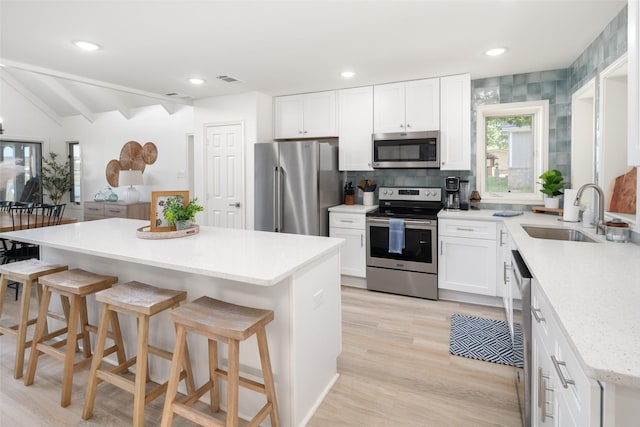 kitchen featuring appliances with stainless steel finishes, white cabinetry, a sink, a kitchen island, and a kitchen breakfast bar