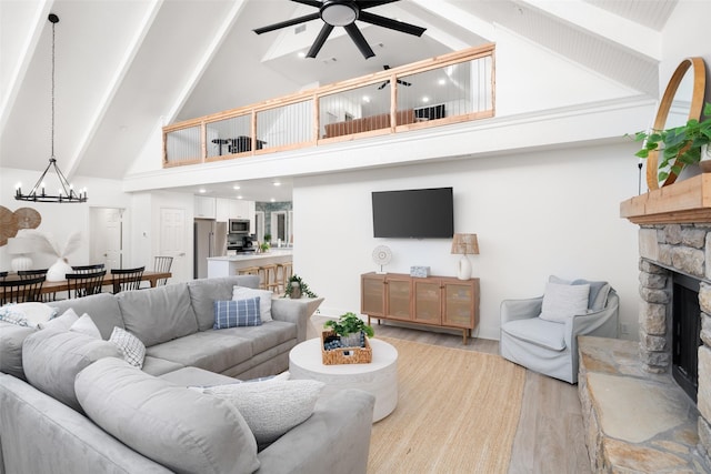 living area featuring high vaulted ceiling, ceiling fan with notable chandelier, a fireplace, light wood finished floors, and beamed ceiling