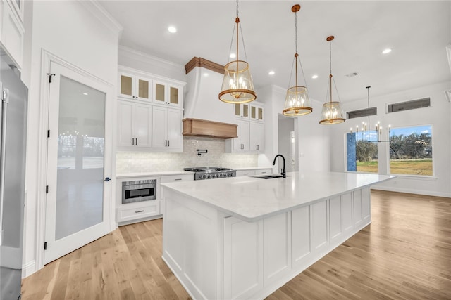 kitchen with a sink, white cabinetry, custom exhaust hood, and stainless steel microwave