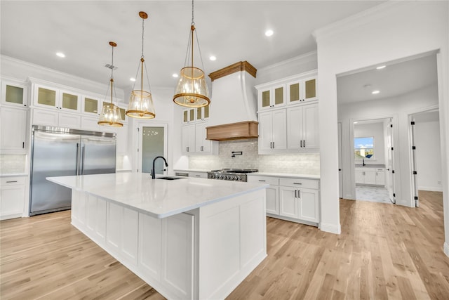 kitchen with stove, built in refrigerator, custom exhaust hood, light countertops, and a sink