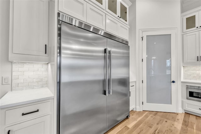 kitchen with tasteful backsplash, light countertops, light wood-style floors, white cabinets, and built in refrigerator