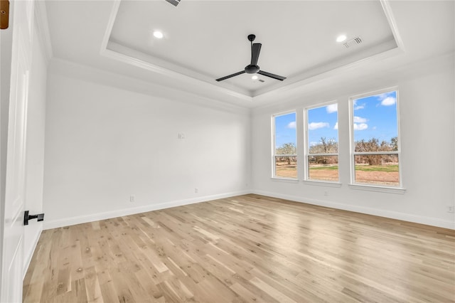 spare room with a ceiling fan, a tray ceiling, visible vents, and light wood-style flooring