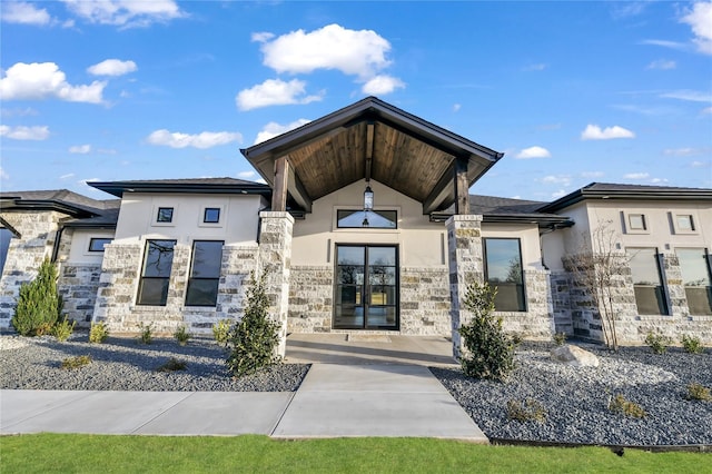 view of exterior entry with stone siding, french doors, and stucco siding