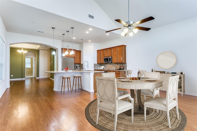 dining room featuring visible vents, arched walkways, lofted ceiling, light wood-style flooring, and ceiling fan with notable chandelier