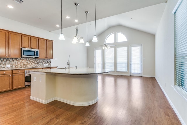 kitchen with light wood finished floors, tasteful backsplash, appliances with stainless steel finishes, brown cabinetry, and a sink