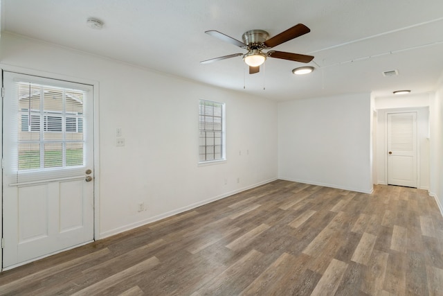 unfurnished room with a ceiling fan, wood finished floors, visible vents, and baseboards