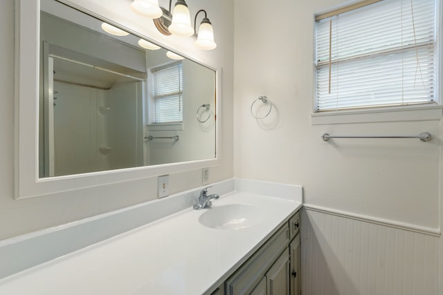 bathroom with a wainscoted wall, walk in shower, and vanity