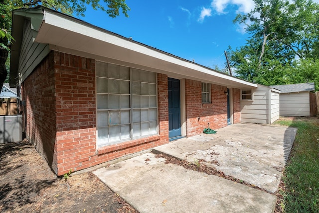 view of front of house featuring an outbuilding, brick siding, a patio, a storage shed, and cooling unit