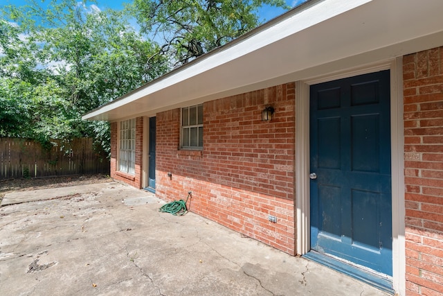 doorway to property featuring a patio area, brick siding, and fence