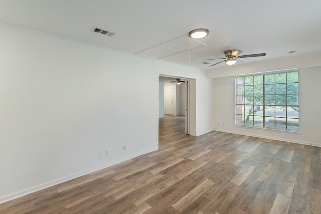 empty room with wood finished floors, a ceiling fan, baseboards, visible vents, and attic access