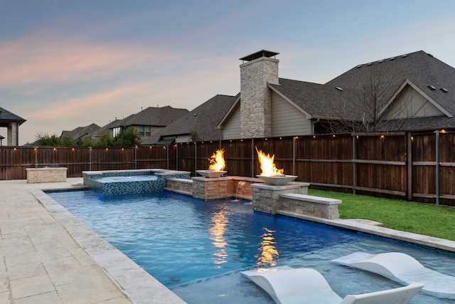 pool at dusk with fence and a pool with connected hot tub