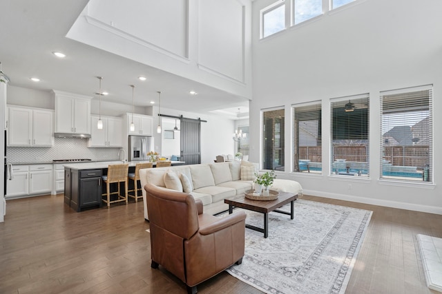 living area featuring a barn door, baseboards, a towering ceiling, dark wood-style floors, and recessed lighting