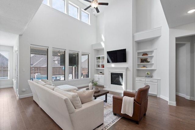 living area with a wealth of natural light, baseboards, dark wood-style flooring, and a glass covered fireplace