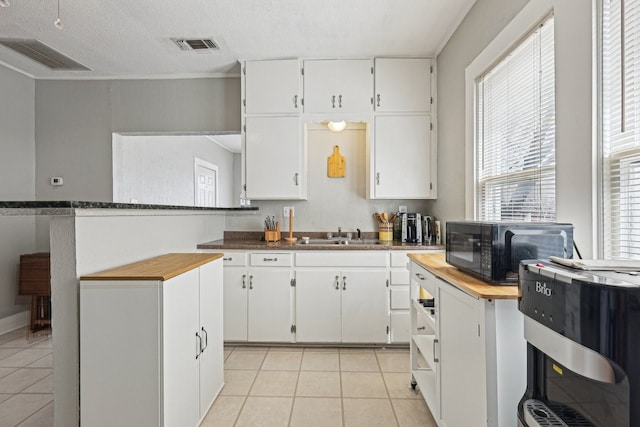 kitchen with light tile patterned floors, visible vents, white cabinetry, a sink, and black microwave