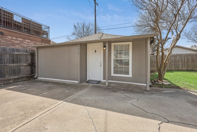 view of front of property with roof with shingles, fence, a patio, and an outbuilding