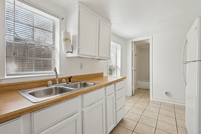 kitchen with light tile patterned floors, freestanding refrigerator, white cabinets, a sink, and a textured ceiling