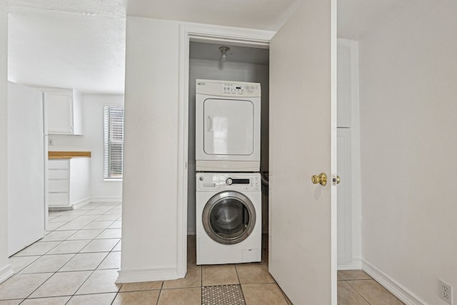 laundry area featuring stacked washing maching and dryer, baseboards, light tile patterned floors, and laundry area