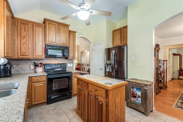 kitchen featuring arched walkways, light tile patterned flooring, backsplash, black appliances, and brown cabinetry