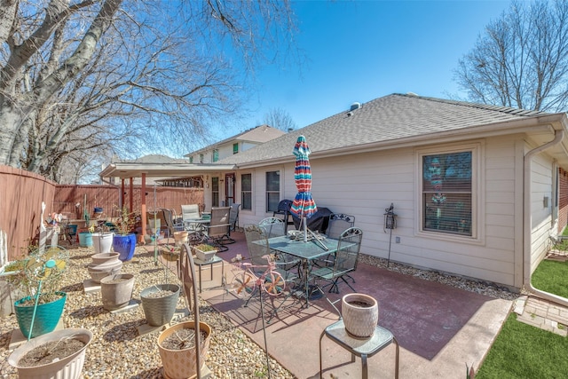 rear view of house featuring a shingled roof, outdoor dining space, a patio area, and fence