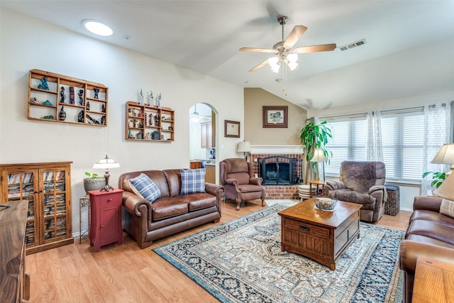 living area featuring visible vents, arched walkways, a ceiling fan, light wood-style flooring, and a fireplace