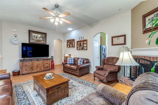 living room featuring arched walkways, a brick fireplace, and wood finished floors