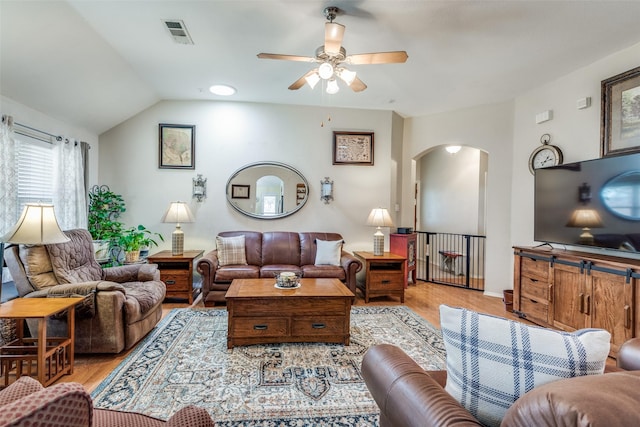 living room featuring arched walkways, lofted ceiling, visible vents, a ceiling fan, and light wood-type flooring