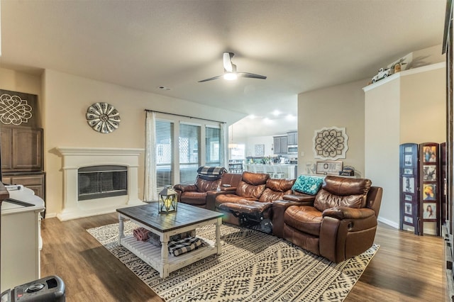 living room with a fireplace with raised hearth, ceiling fan, dark wood-type flooring, and baseboards