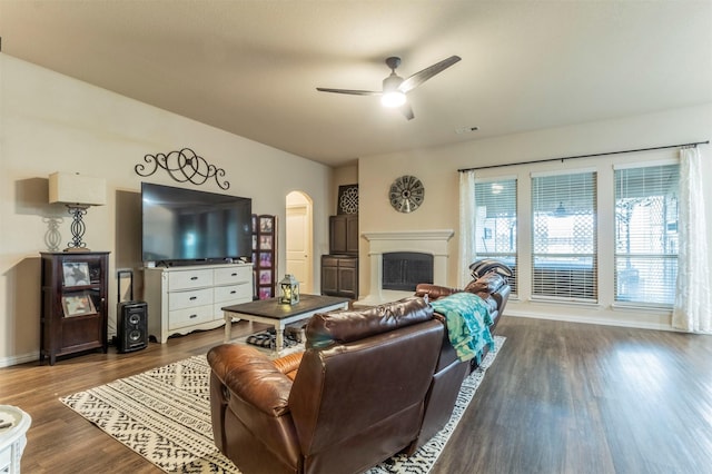 living room with arched walkways, a fireplace, visible vents, a ceiling fan, and dark wood finished floors