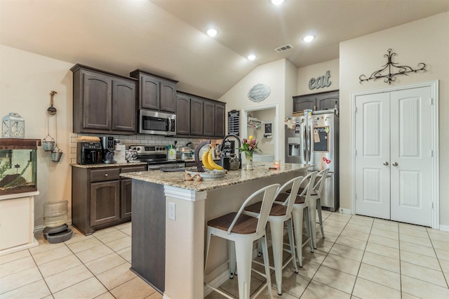 kitchen featuring dark brown cabinetry, light tile patterned floors, an island with sink, a breakfast bar, and stainless steel appliances