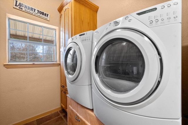 laundry area featuring dark tile patterned flooring, washing machine and clothes dryer, cabinet space, and baseboards