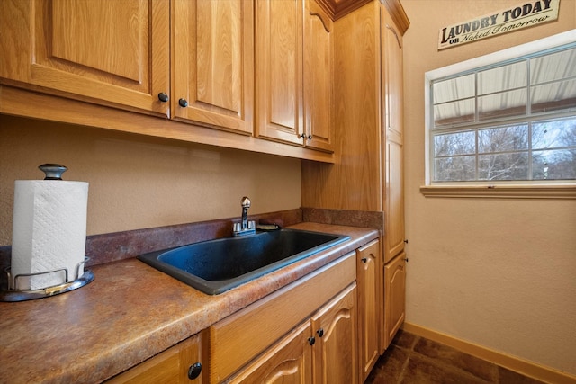 kitchen featuring baseboards, brown cabinetry, and a sink