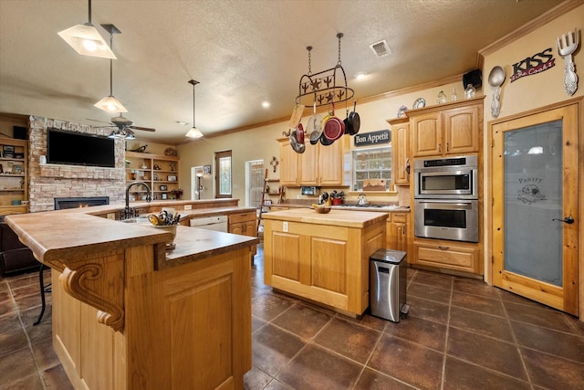 kitchen featuring double oven, a stone fireplace, visible vents, open floor plan, and a large island with sink