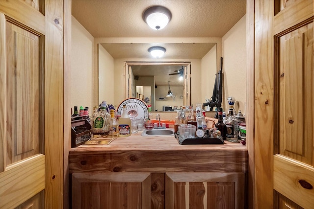 bar with a textured ceiling, indoor wet bar, and a sink