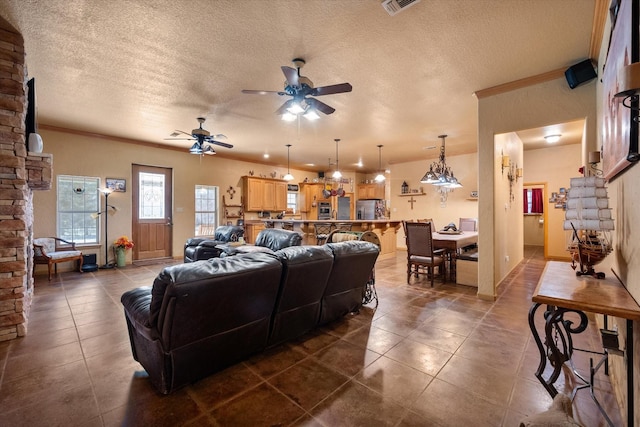 living room featuring a ceiling fan, dark tile patterned floors, ornamental molding, and a textured ceiling