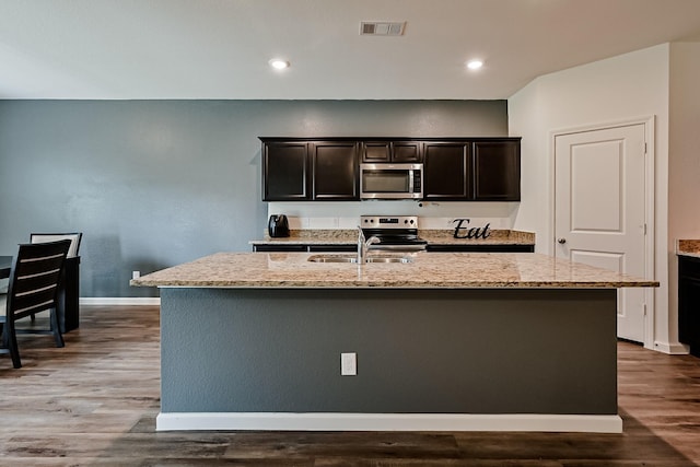 kitchen with light stone counters, a kitchen island with sink, stainless steel appliances, a sink, and visible vents