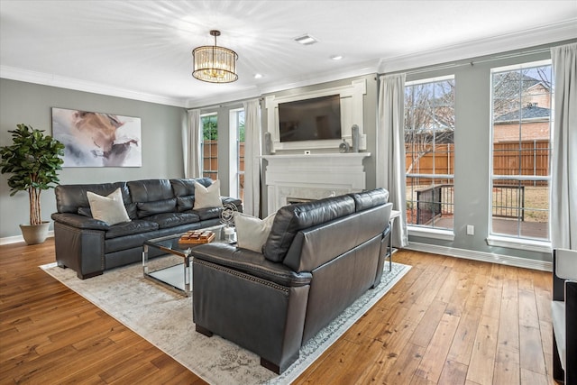 living room with crown molding, baseboards, a fireplace, hardwood / wood-style flooring, and a notable chandelier