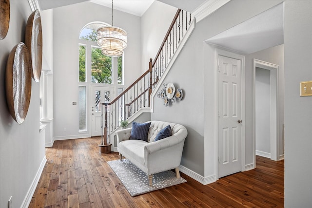 entryway featuring hardwood / wood-style flooring, an inviting chandelier, baseboards, a towering ceiling, and stairs