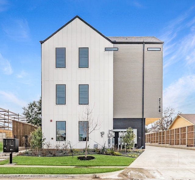 modern inspired farmhouse with concrete driveway, a front lawn, board and batten siding, and fence