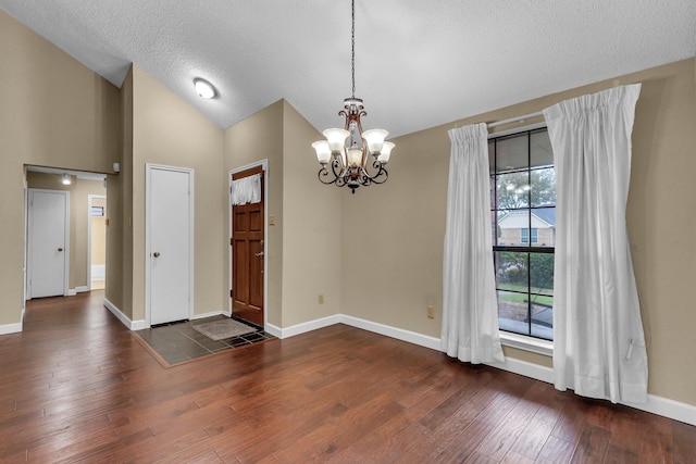 interior space featuring an inviting chandelier, vaulted ceiling, a textured ceiling, wood finished floors, and baseboards