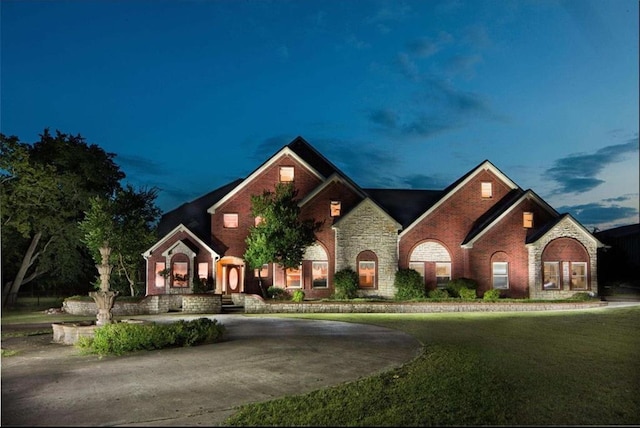 view of front of house with a front yard, curved driveway, and brick siding